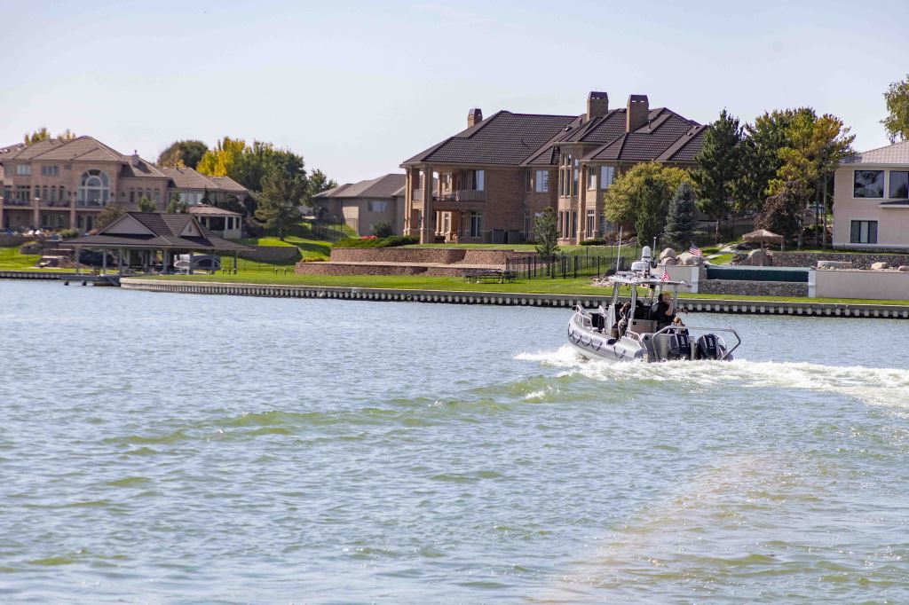 A motorboat navigating a lake, with upscale homes and manicured lawns in the background.