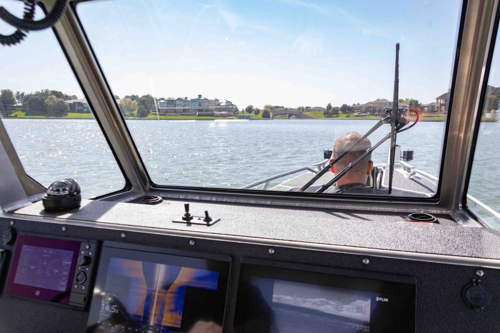 View from the cockpit of a boat, showing the water and a person navigating while large houses line the shore.