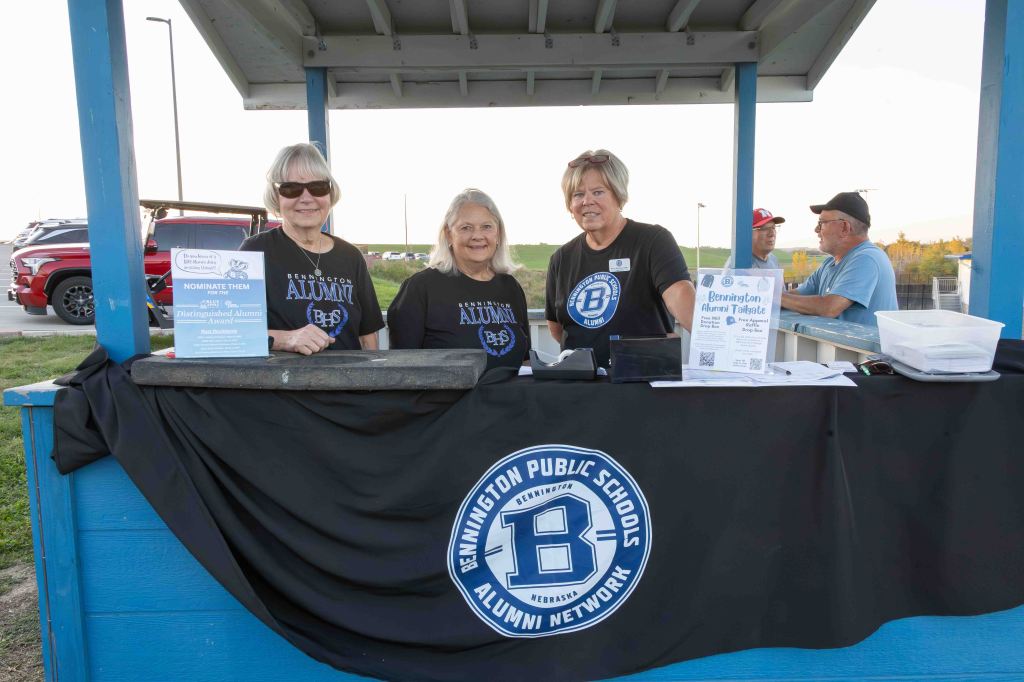 Three women at a table promoting the Bennington Public Schools Alumni Network at an outdoor event, with informational materials displayed.