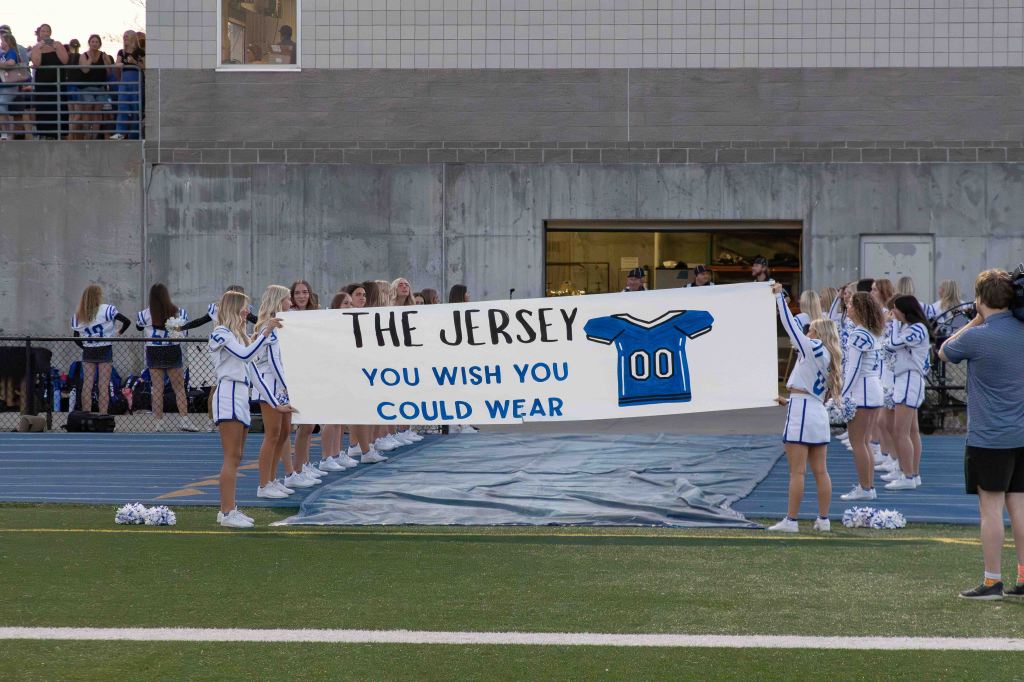 Cheerleaders holding a large banner that reads 'THE JERSEY YOU WISH YOU COULD WEAR' at a sports event.