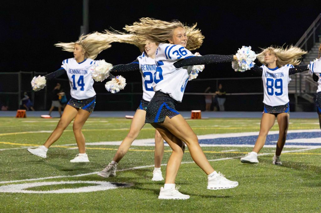 Cheerleaders performing on a football field, wearing blue and white uniforms, and dancing with pom-poms.