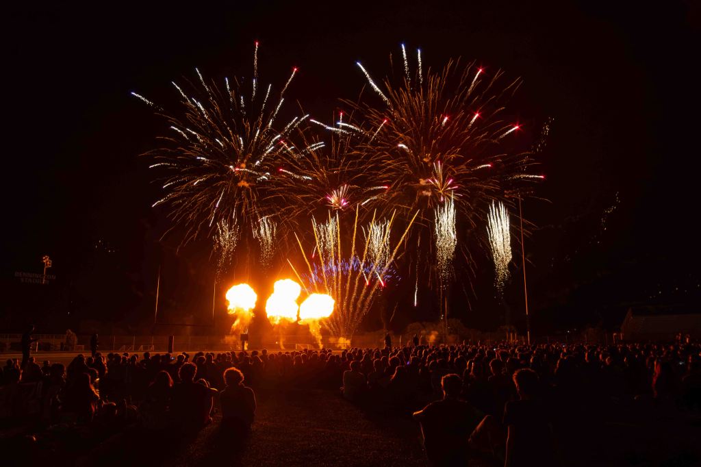 A crowd watching a vibrant fireworks display at night, with colorful sparks illuminating the dark sky.