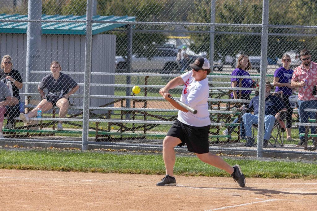 A young athlete swings a baseball bat during a game, with spectators sitting in the background watching the action.