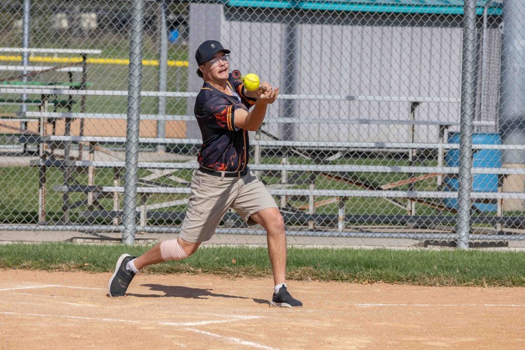 A young athlete in a baseball uniform catching a softball at a sports field.