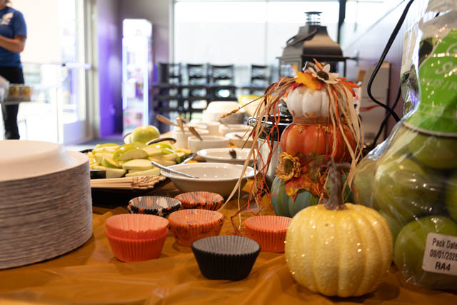 A decorated table with various bowls, colored cupcake liners, fresh green apples, and a collection of pumpkins, including a glittery yellow one, set against a backdrop of a dining area.