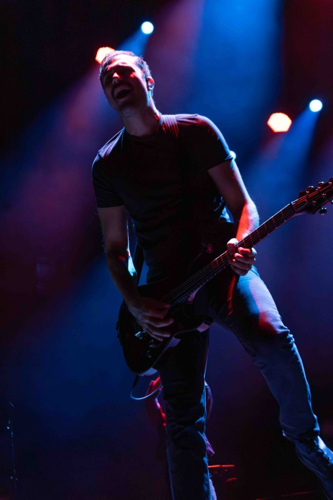 A guitarist performing on stage with dramatic lighting, passionately playing and singing into a microphone.