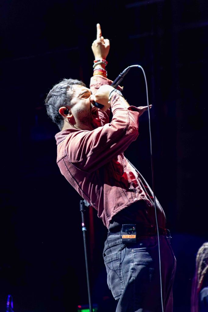A male singer passionately performing on stage, holding a microphone in one hand and raising the other hand with an outstretched finger.