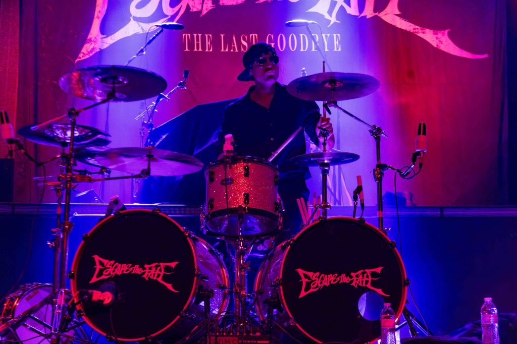 A drummer performing on stage with colorful lighting, playing with enthusiasm during a concert.