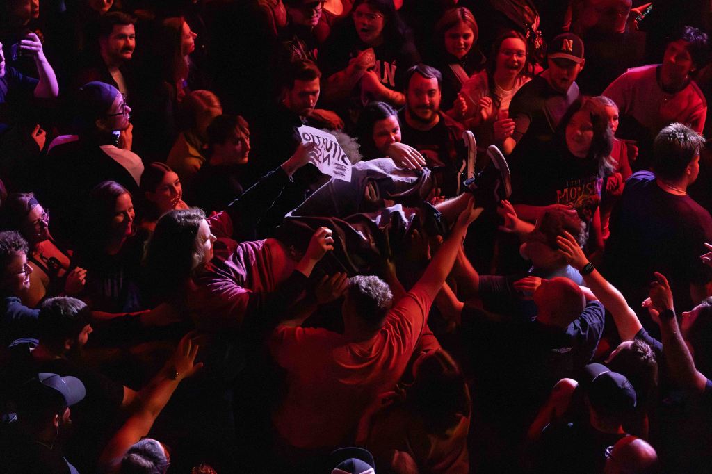 A crowd at a concert enjoying the performance, with one individual crowd surfing while others reach out to support them.
