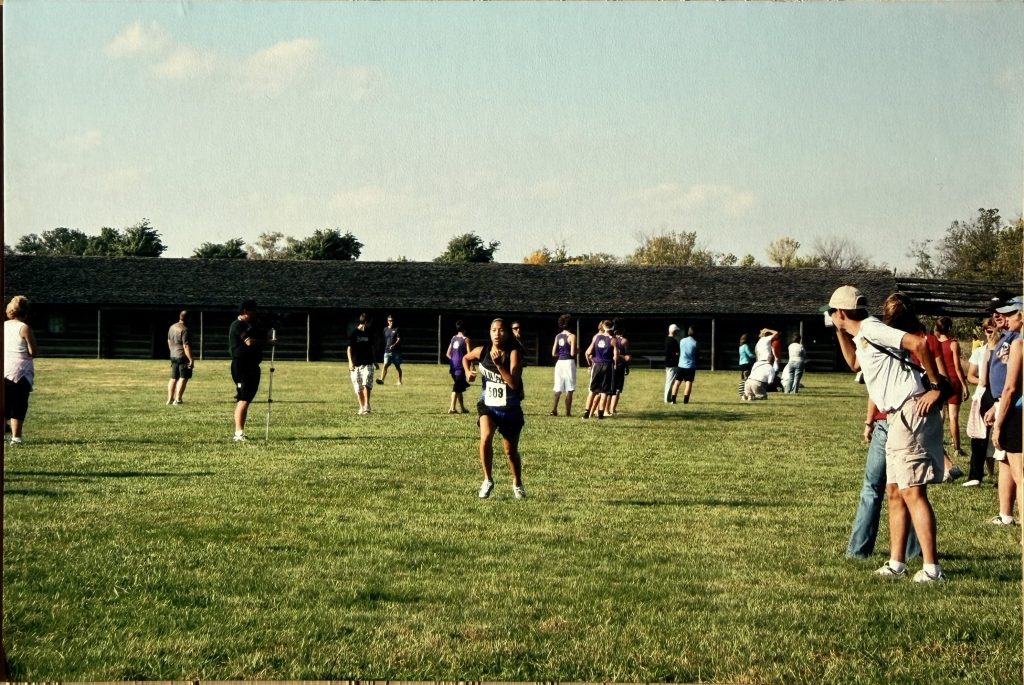 A group of people participating in an outdoor event, with some individuals running and others watching in a grassy field.