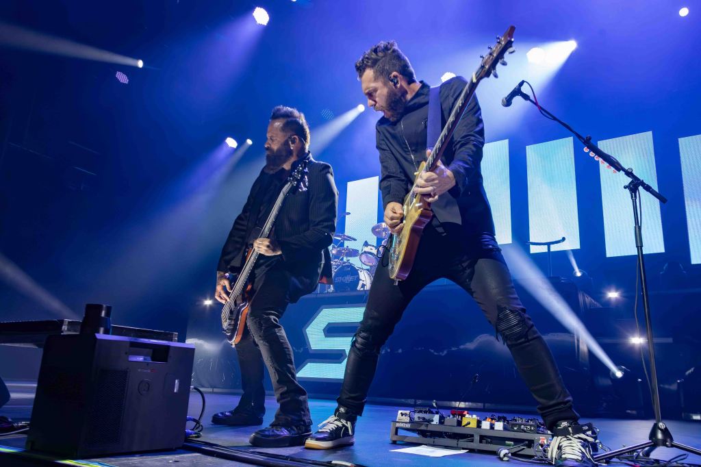 Two musicians performing on stage with guitars under dramatic lighting.