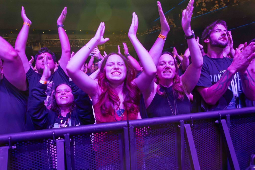 A crowd of enthusiastic concertgoers clapping and enjoying the performance, with individuals displaying excitement and joy against a backdrop of colorful stage lighting.