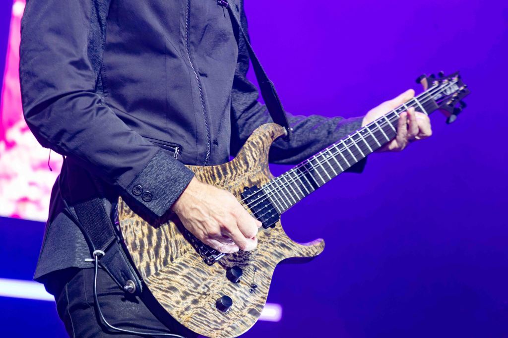 Close-up of a musician's hand playing an electric guitar with a unique, patterned body against a colorful background.