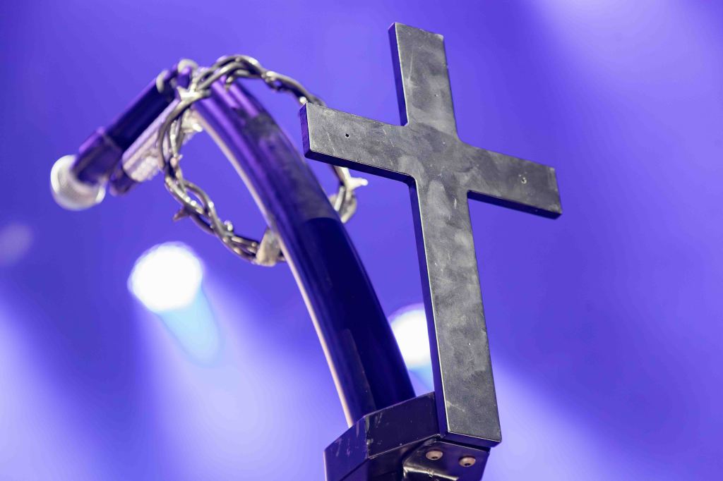 Close-up of a microphone stand featuring a black cross design, with a purple background and soft stage lighting.