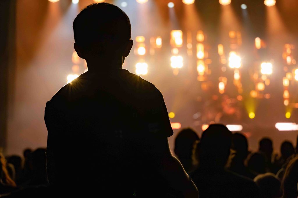 Silhouette of a child watching a concert with bright stage lights in the background.