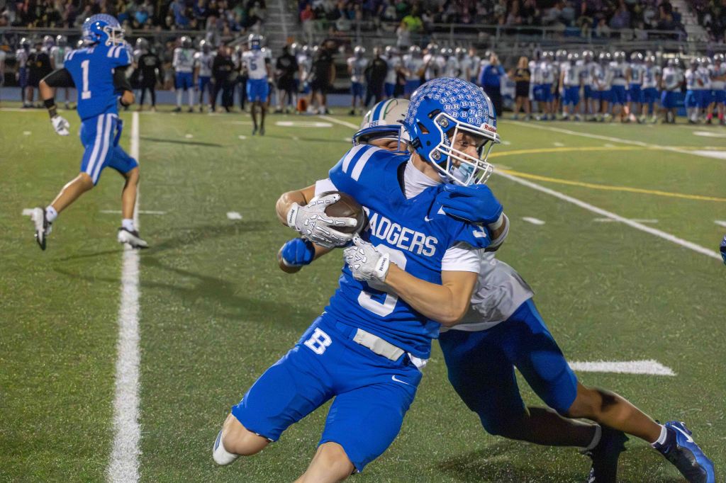 A football player in a blue uniform labeled 'Badgers' evades a tackle from an opponent, while another player in the background runs on the field.