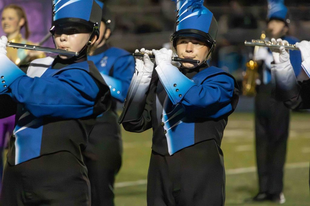 A marching band member playing the flute wearing a blue and black uniform and a matching hat.